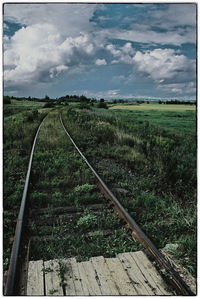 Road passing through field against cloudy sky