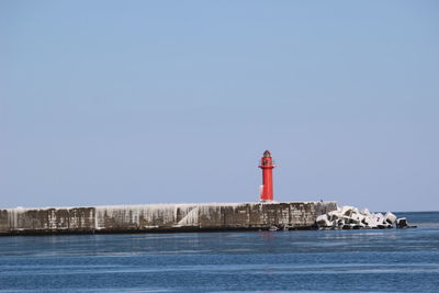 Lighthouse by sea against clear sky