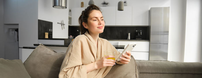 Young woman using mobile phone while sitting on sofa at home