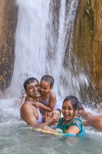Cheerful parents with son enjoying waterfall