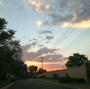 Road by silhouette trees against sky during sunset