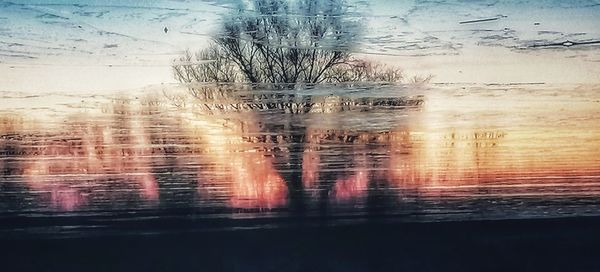 Digital composite image of bare trees by lake against sky