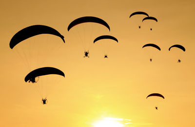 Low angle view of silhouette people paragliding against sky during sunset