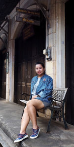 Portrait of woman sitting on bench against building