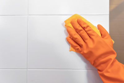 Close-up of hand holding orange against white wall