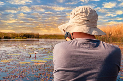 Young photographer man with a hat rides a traditional mokoro on the okavango delta and takes picture