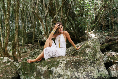 Beautiful young woman sitting on rock in forest