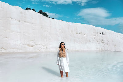 Full length portrait of young woman standing against sky