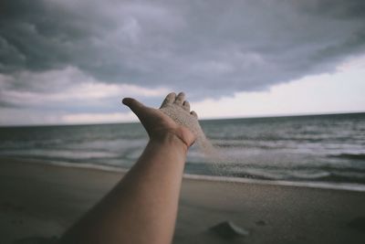 Close-up of hand holding lizard on beach against sky
