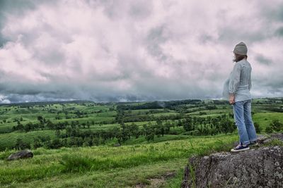 Man standing on landscape against cloudy sky
