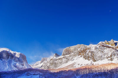 Low angle view of snowcapped mountains against blue sky