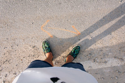 Low section of man standing by double arrow symbol on road