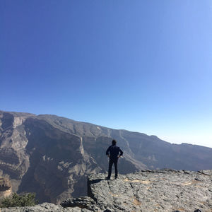Man standing on cliff looking at mountains against clear blue sky