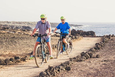 Couple riding bicycles at beach against clear sky