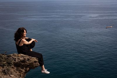 Side view of young woman sitting on rock by sea