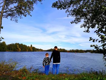 Rear view of teenage boy standing with brother by lake