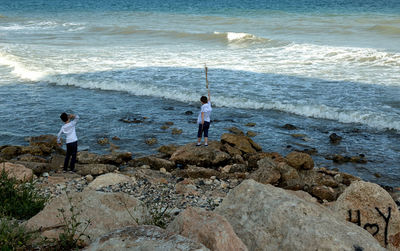 High angle view of boys standing on rocks at beach