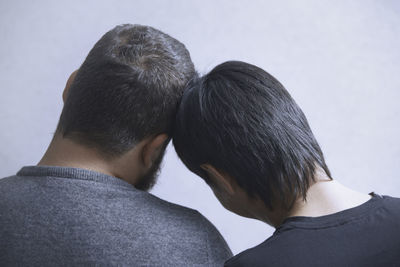 Rear view of gay couple relaxing by white wall at home