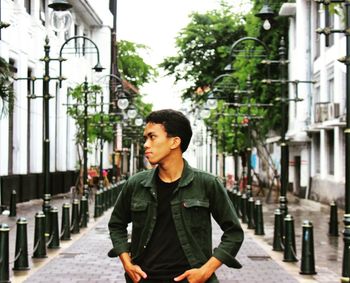 Young man looking away while standing on street in city