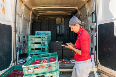 Concentrated female gardener in bandana browsing cellphone while working in farm and looking at screen