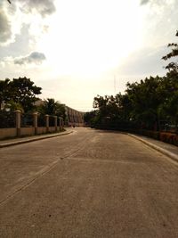 Empty road amidst trees and buildings against sky