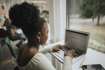 Side view of female student using laptop at table in university