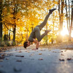 Side view of man doing handstand on road during autumn