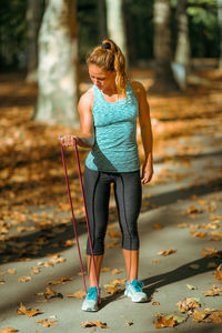 Woman exercising biceps with elastic band outdoors in the fall, in public park