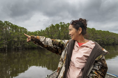 Smiling senior woman pointing away while standing on boat in lake