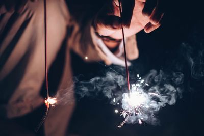 Midsection of woman holding sparkler at night