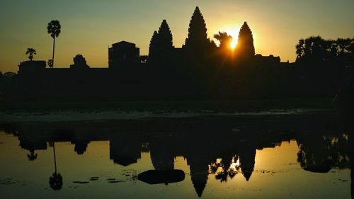 Silhouette buildings by lake against sky during sunset