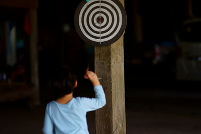 Rear view of boy throwing darts at dartboard at night