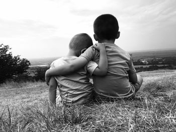 Rear view of friends sitting on field against sky