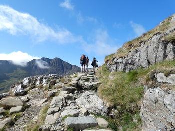 People walking on rocks in mountains against sky