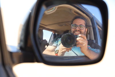 Portrait of man photographing through mirror while sitting in car