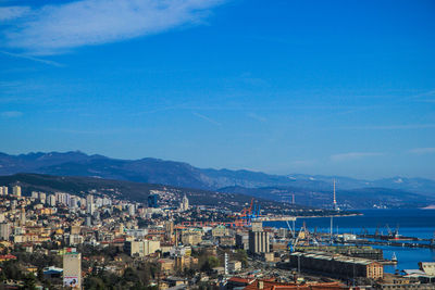 High angle view of city by sea against blue sky