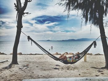 Man using mobile phone while resting in hammock at beach