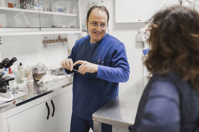 Positive adult male doctor in uniform talking with crop woman in laboratory