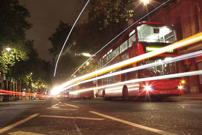 Light trails by buses on street at night