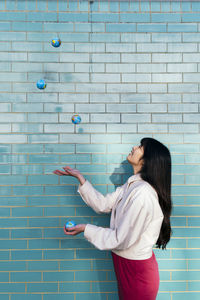 Young woman juggling with globes by turquoise brick wall