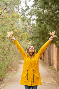 Cheerful woman holding autumn leaves standing outdoors