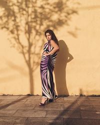 Young woman standing on sidewalk against wall