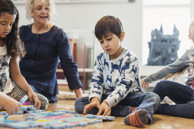 Female teacher and children playing jigsaw puzzle