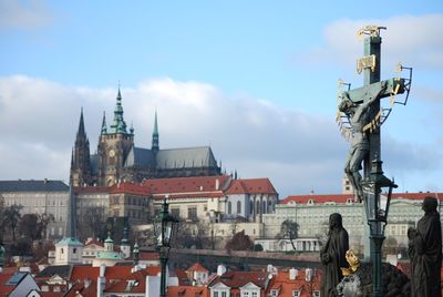 Crucifix at charles bridge against buildings and sky