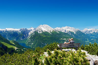 Couple sitting on a bench in front of the alps enjoying the mountain panorama