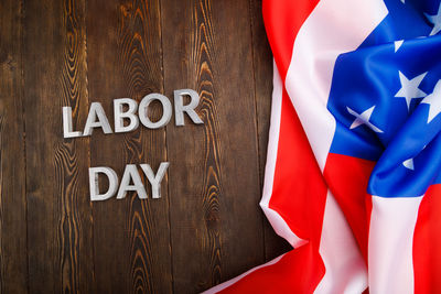 Words labor day laid with silver metal letters on wooden surface with crumpled usa flag on left side