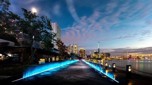 Illuminated street amidst buildings against sky at night