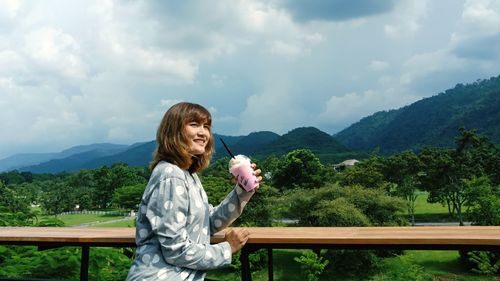 Woman holding drink against mountains