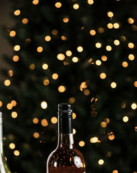 Close-up of a wine bottle in front of illuminated christmas tree 