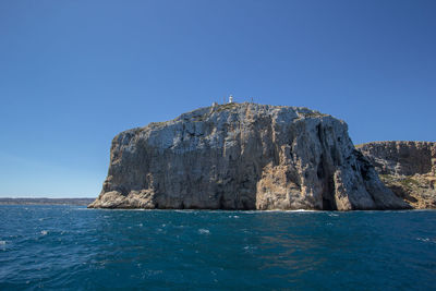 Rock formations by sea against clear blue sky